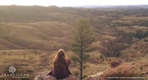 Student sitting along a ridge looking out over a rural valley at sunset